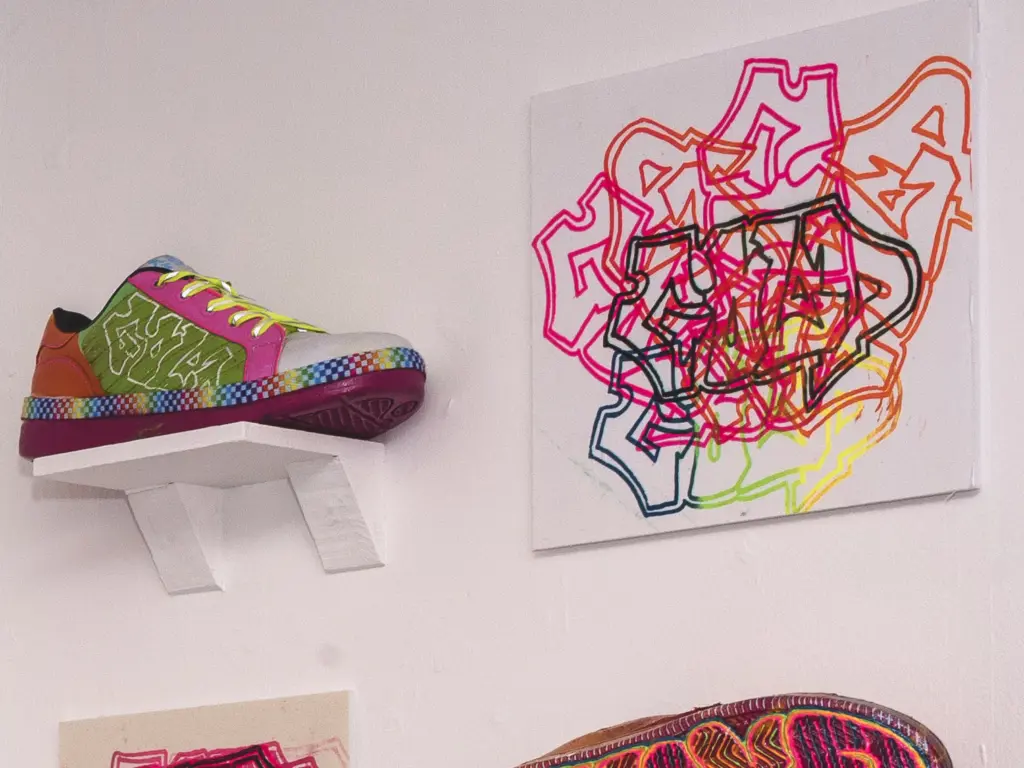 An art piece produced by a HCA Art, Design and Communication student comprising of brightly decorated trainers and graffiti art.