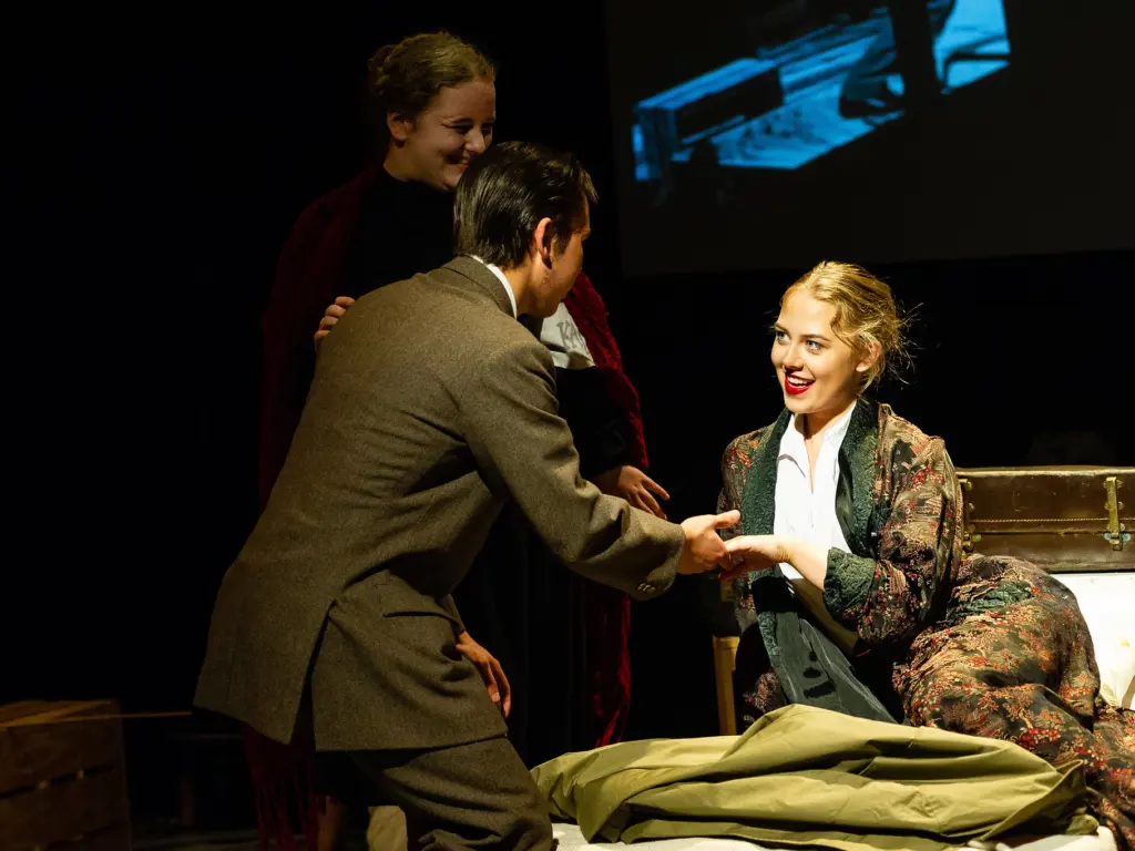 A trio of HCA performing arts students mid performance, the three actors lit under a spotlight at a pivotal moment.