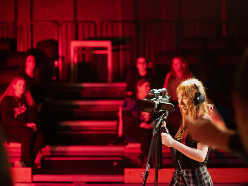 An HCA Creative Media student filming in the Folly Arts Theatre under deep red lighting.