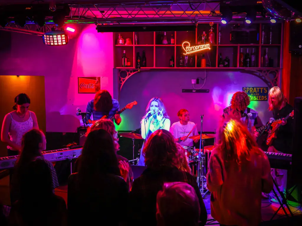 An band made of up HCA music students performs at a bar under pink and blue neon lighting.