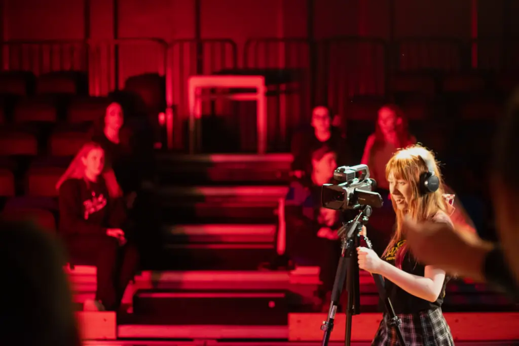 An HCA Creative Media student filming in the Folly Arts Theatre under deep red lighting.