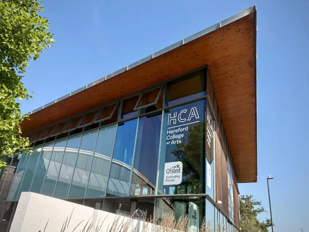 The Folly Lane Campus building from outside on a sunny day, the HCA and Ofsted Outstanding logos prominently displayed on the windows.