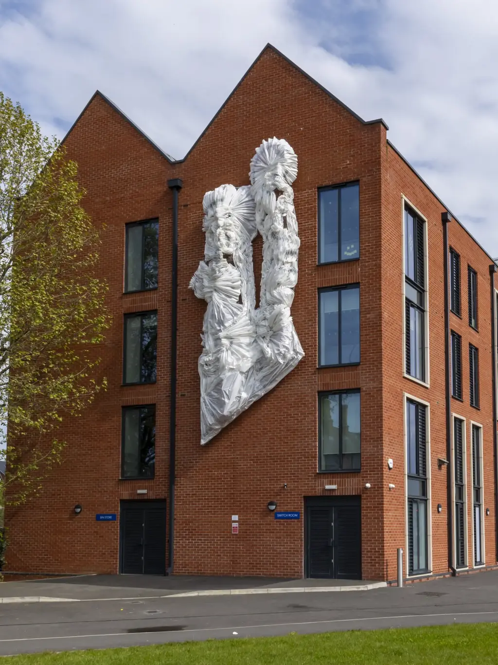 Image of student halls exterior featuring a sculpture from artist Laura White and grass in the foreground