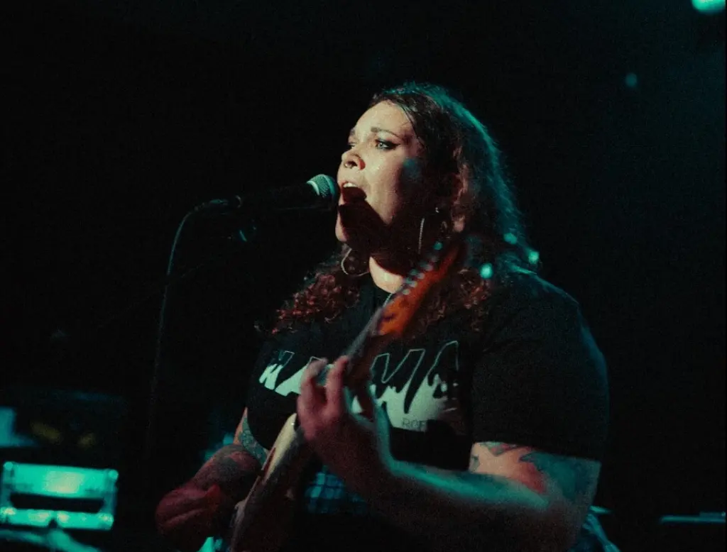 Portrait of Zoe Collins, she is playing her guitar under green stage lighting.