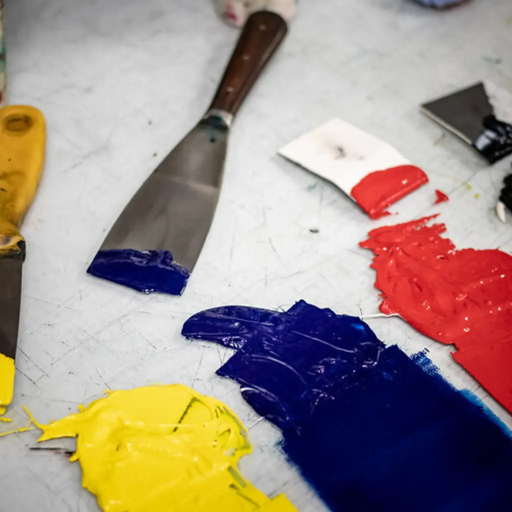 A variety of different coloured inks spread onto a glass plate with the corresponding palette knives sat beside.