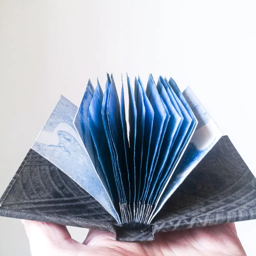 A hand holding up a small blue book, with it's pages fanned out.
