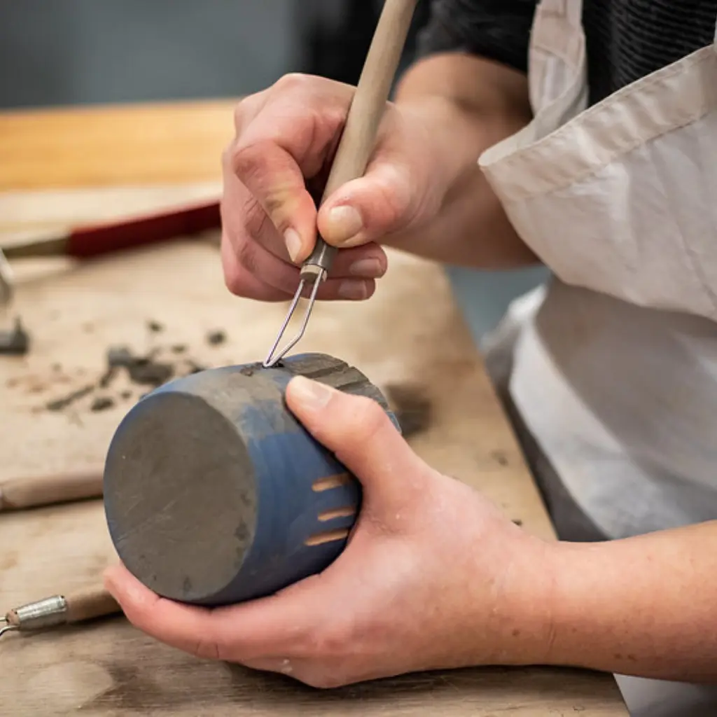 A close-up photo of a student carving into a blue ceramic pot.