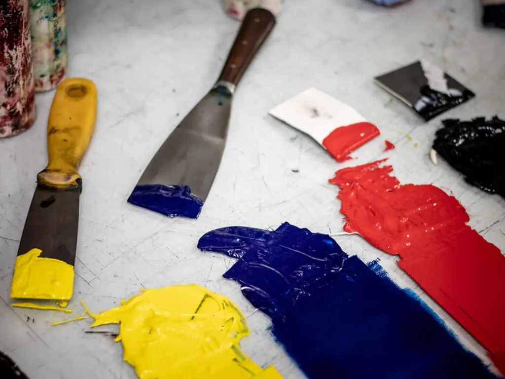 A variety of different coloured inks spread onto a glass plate with the corresponding palette knives sat beside.