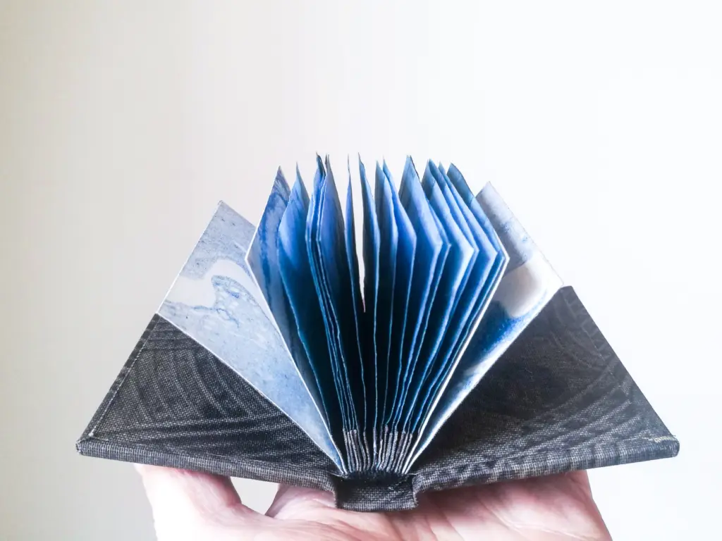 A hand holding up a small blue book, with it's pages fanned out.