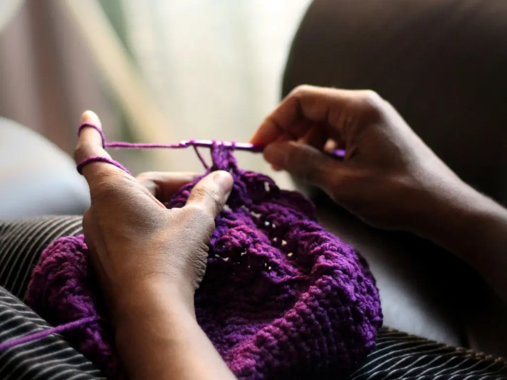 A close-up of someone crocheting a beanie with purple wool.