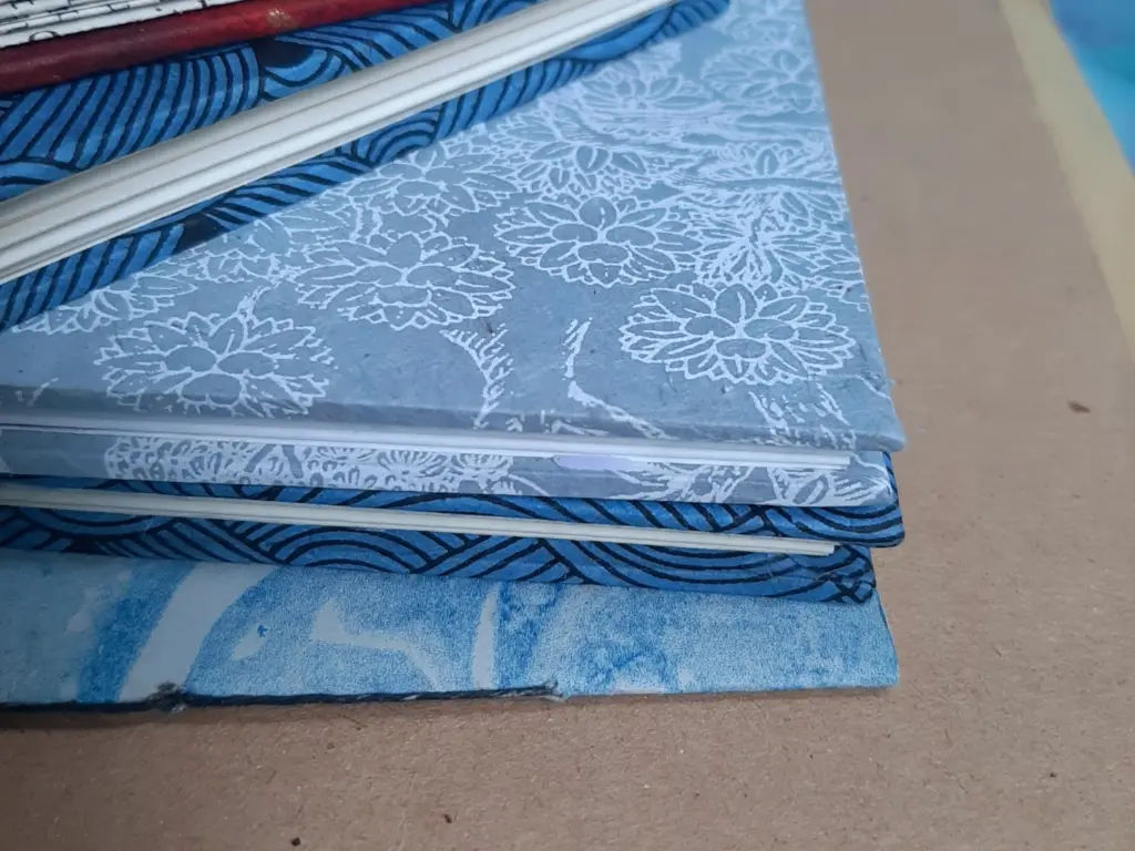 A close-up stack of hand-made notebooks with different colour binding.