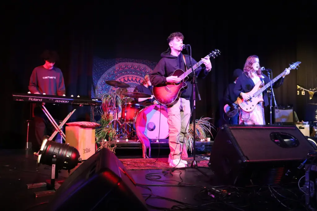 4 young people playing music on a lit stage.