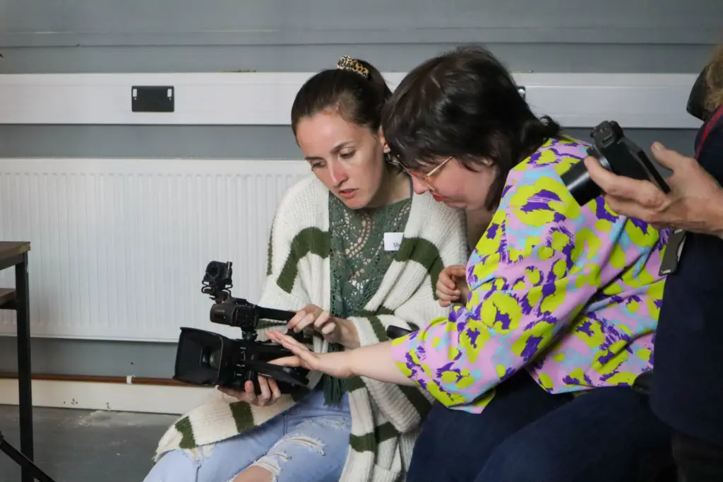 Two women looking at a video camera, working together.