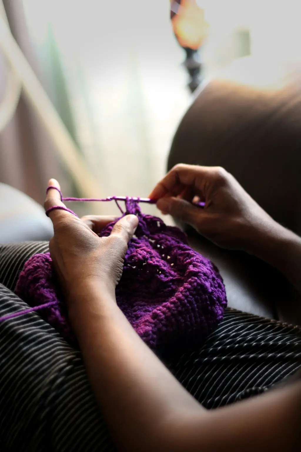 A close-up of someone crocheting a beanie with purple wool.