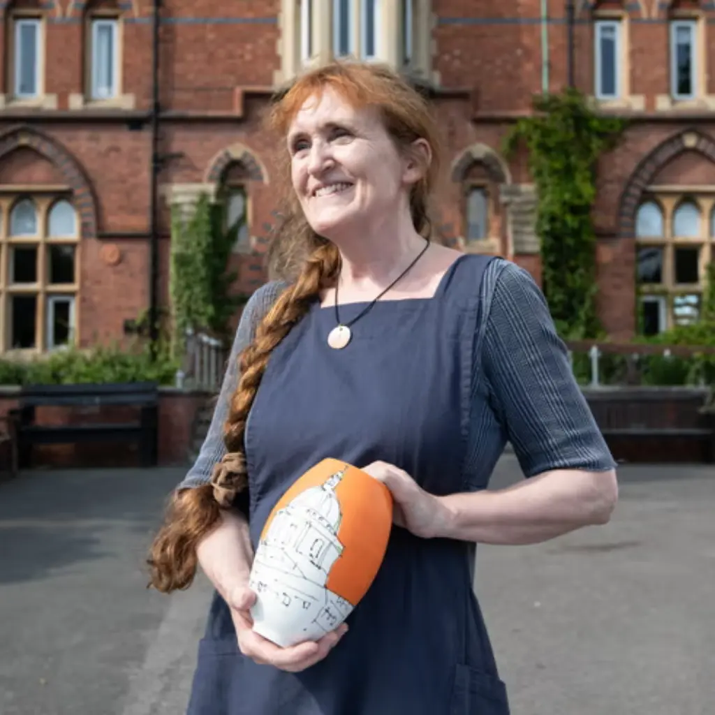 Photo of Linda holding a piece of her orange and white ceramics, in front of the HCA campus.