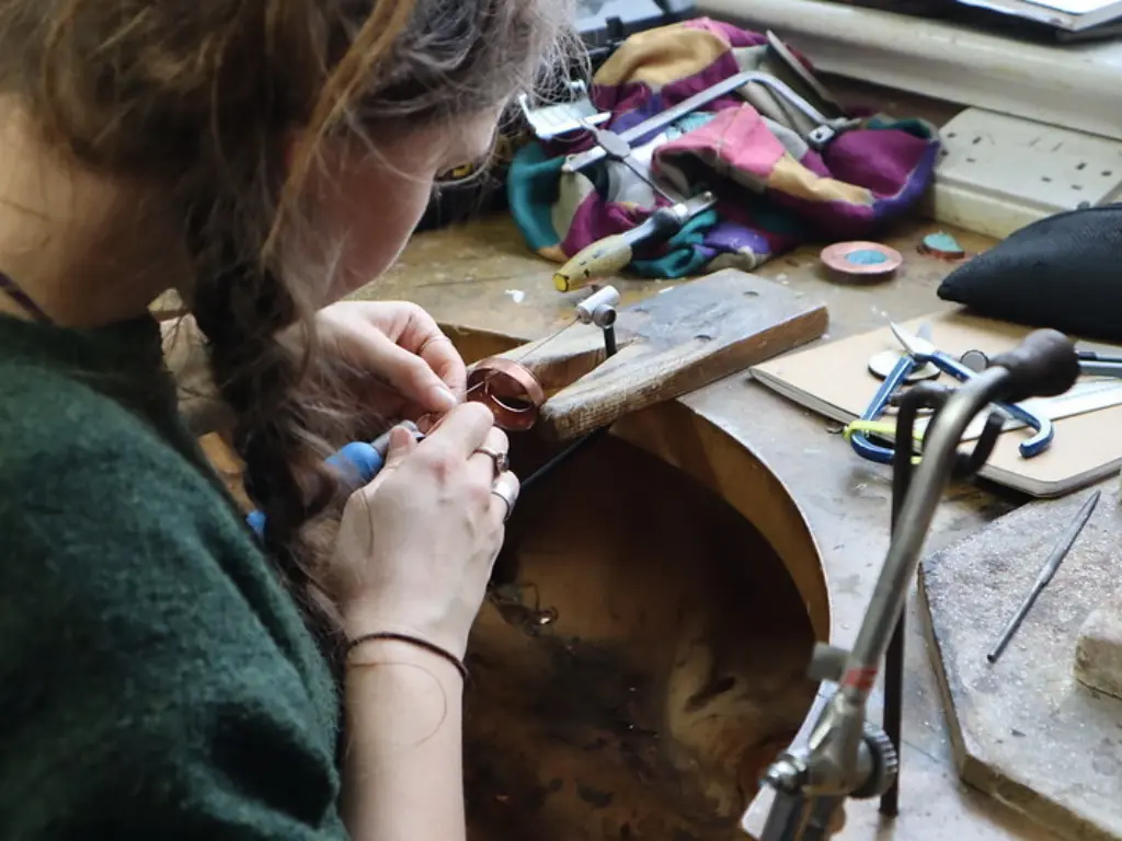 An over-the-shoulder shot of a young woman working at a small metals bench.