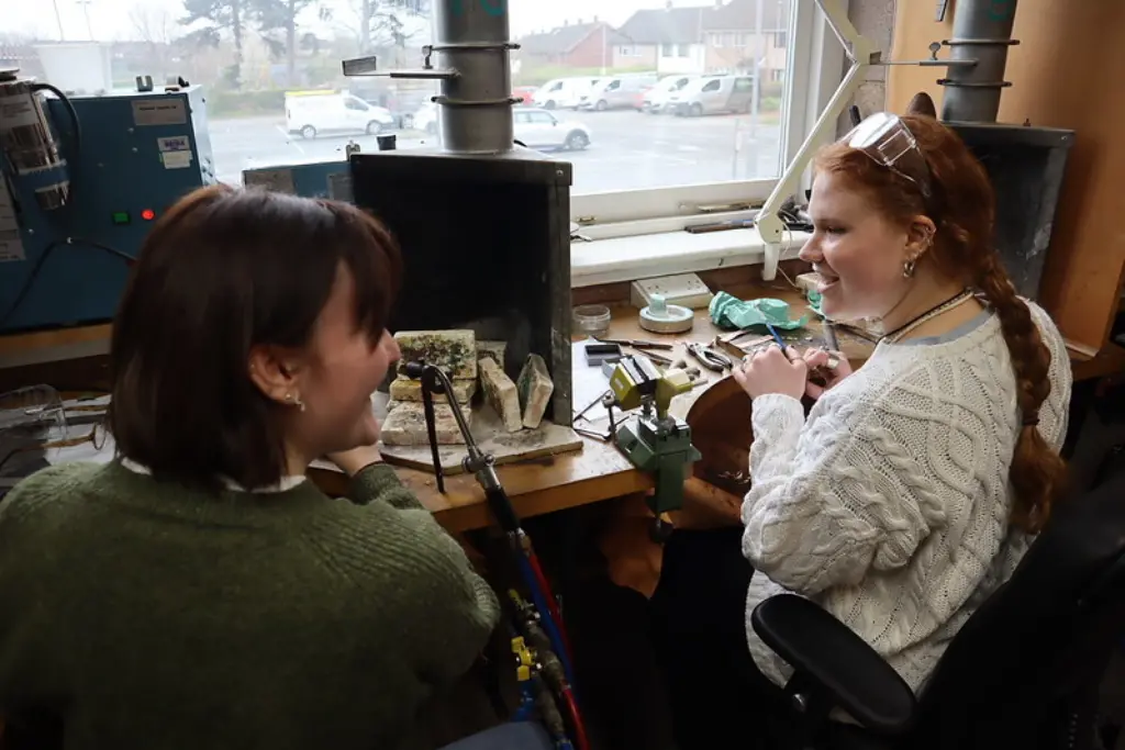 Two girls smiling and chatting with each other whilst working in the small metals workshop.